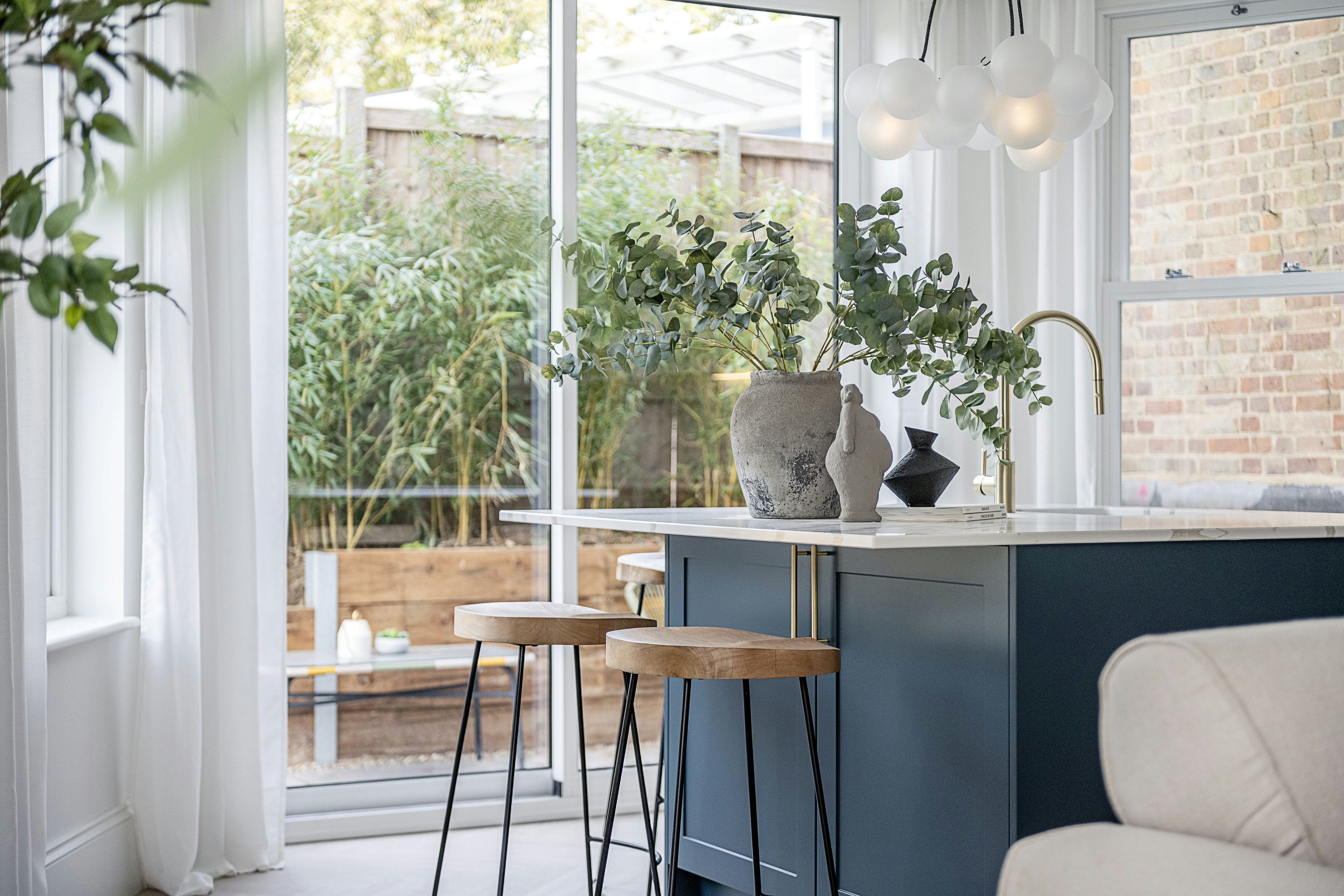 The Rosemont apartment kitchen bar with oak stools, blue island and garden view &mdash; interior design by Ademchic